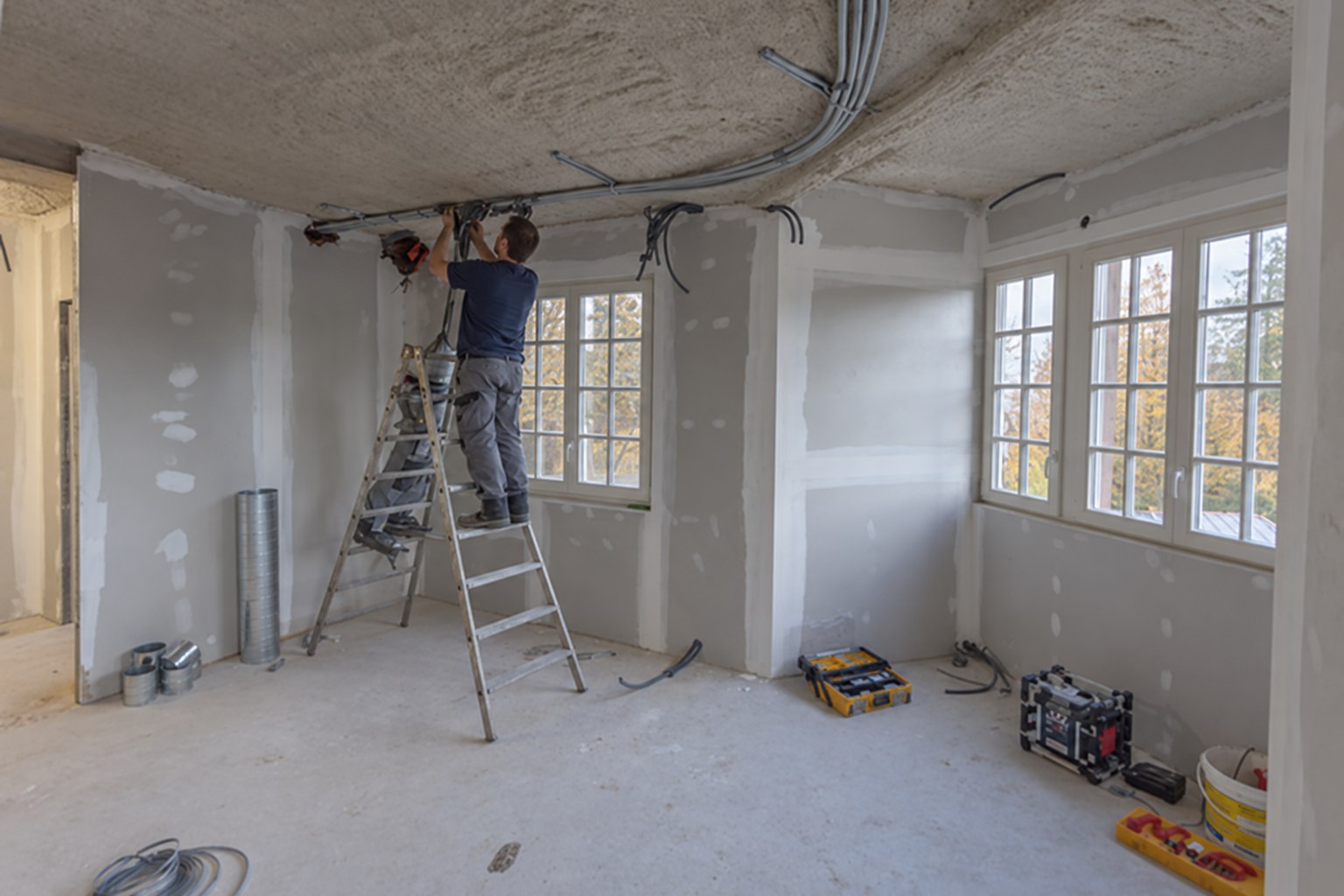 Électricien sur un escabeau près des gaines électriques au plafond d’une pièce en rénovation